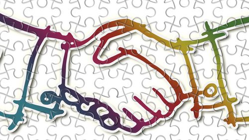 Das Bild zeigt eine stilisierte, bunte Darstellung zweier Hände, die sich miteinander verbinden. Diese symbolisieren Zusammenarbeit und Einheit. Der Hintergrund ist hell und enthält Puzzleteile, die auf das Thema der Verbindung und des Zusammenspiels hinweisen.