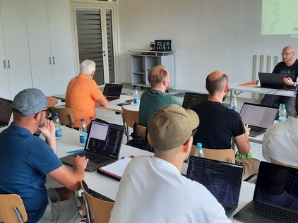 Teilnehmer eines Workshops bei den TYPO3 Developer Days 2024 in Karlsruhe, die an ihren Laptops arbeiten und einem Vortrag zuhören.