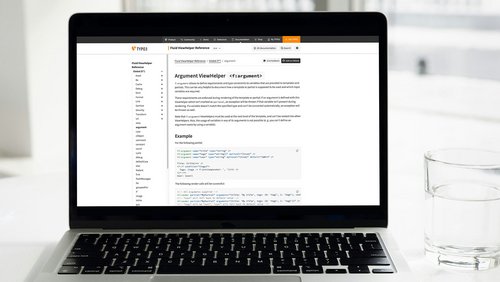 Auf dem Laptop-Bildschirm ist die Dokumentation für den TYPO3 Fluid ViewHelper zu sehen. Der Abschnitt beschreibt den Argument ViewHelper, der Anforderungen und Typen für Variablen in Templates und Partials definiert. Beispielcode veranschaulicht die Verwendung dieser Argumente.