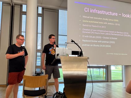 Das Bild zeigt Christian Kuhn (links) und Markus klein (rechts) bei den TYPO3 Developers Days 2024, die vor einer Folie mit dem Titel “CI infrastructure - looking back” sprechen.