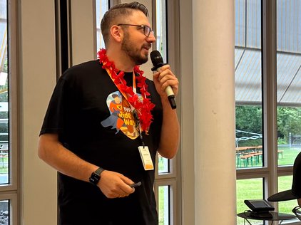 Fabian Stein bei den TYPO3 Developer Days 2024 in Karlsruhe, der die Begrüßungsansprache hält. Er trägt ein schwarzes T-Shirt mit dem Aufdruck ‘TYPO3 Ride the Wave’.